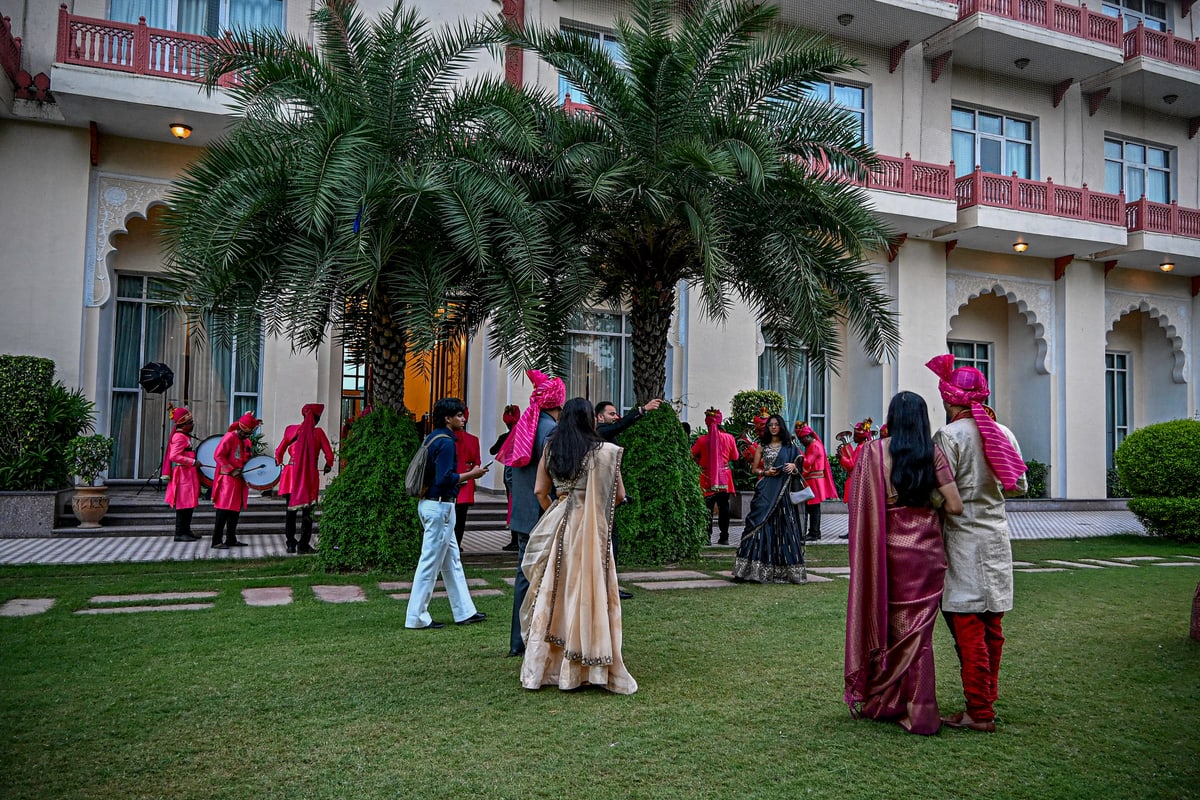 Guests in colorful Indian attire gather on a palace lawn as drummers in red turbans play.
