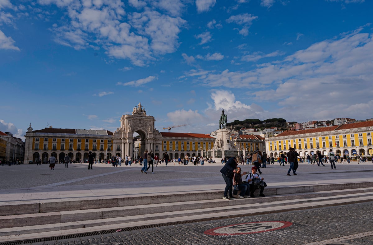 The arch and yellow arcades of Praça do Comércio under a bright sky.