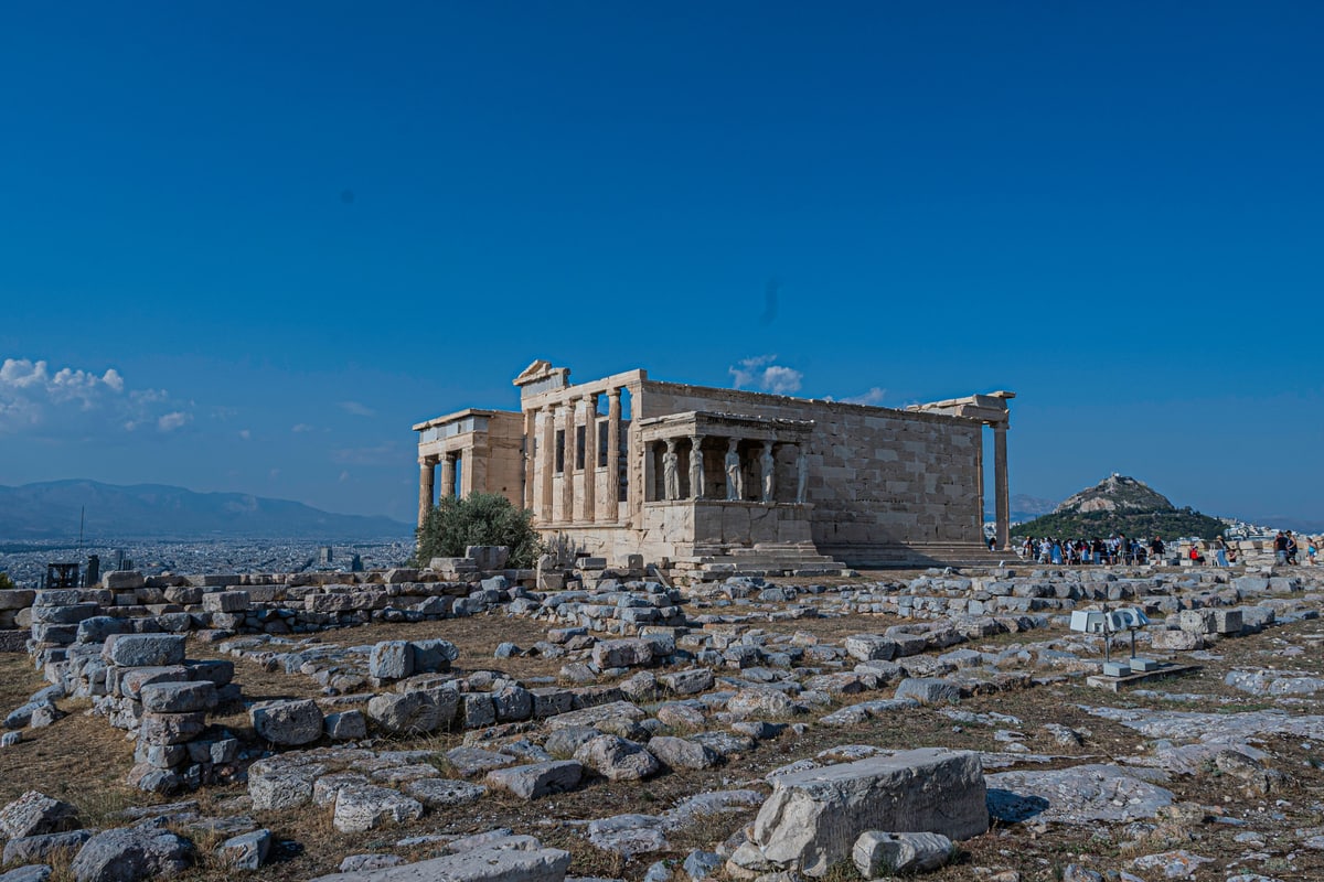 The Erechtheion temple on the Acropolis under a deep blue sky, ruins scattered in front.