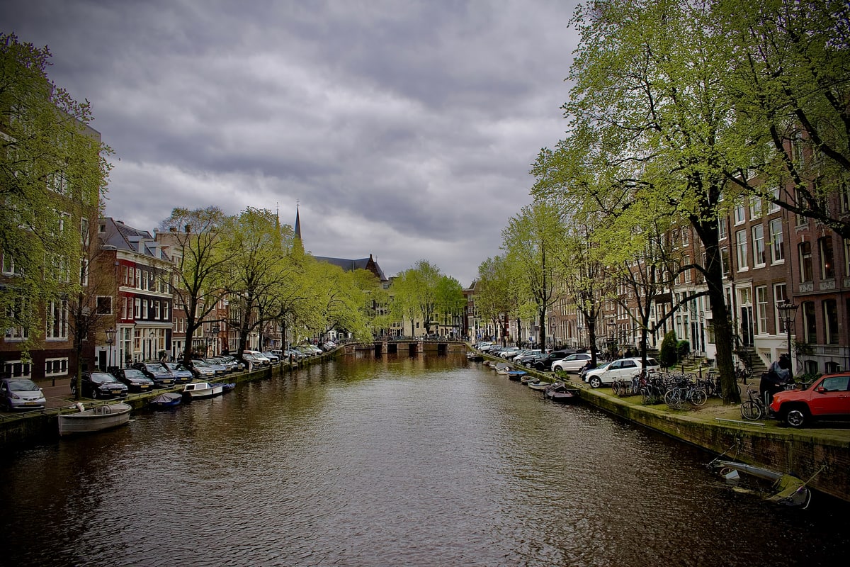 A quiet canal under grey clouds with spring trees along both banks.