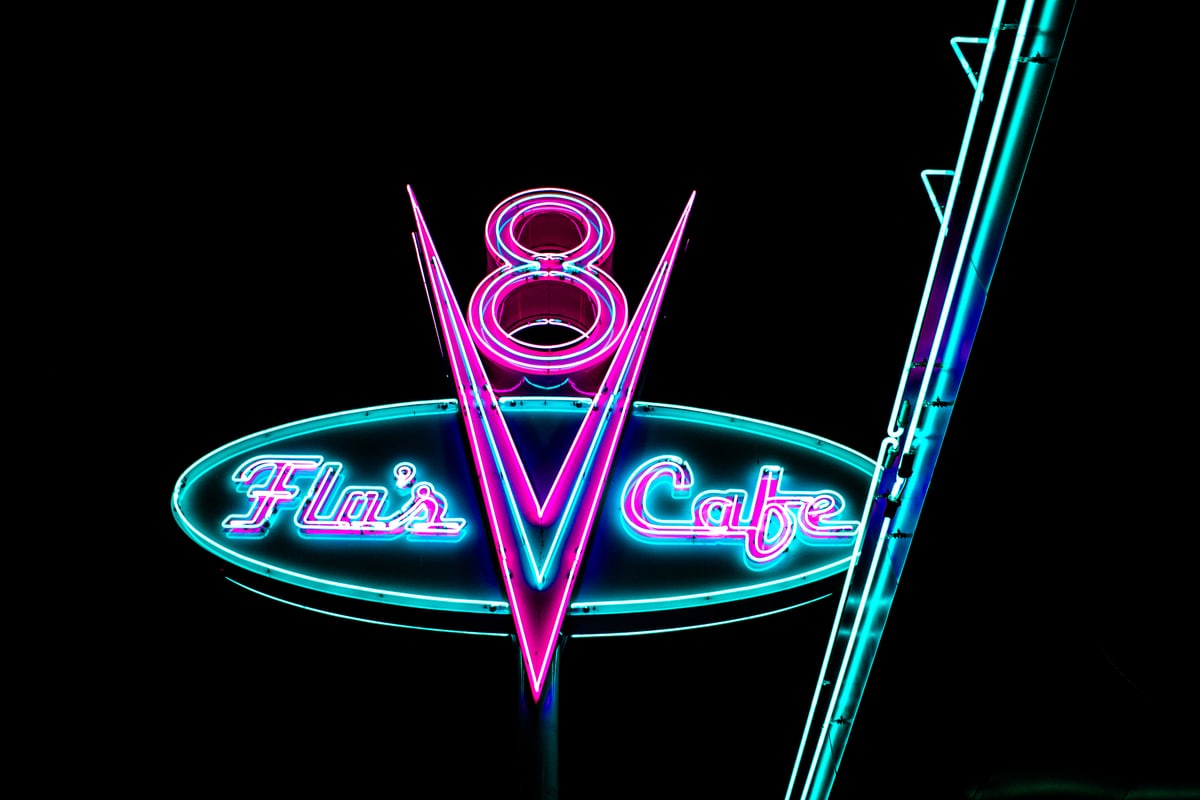 A pink and teal neon V8 sign against the black night sky.