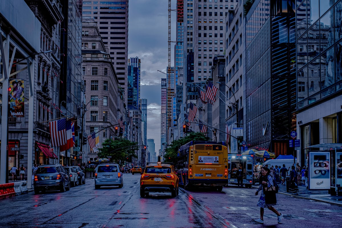 Yellow cabs and a school bus on a wet Manhattan avenue lined with flags.