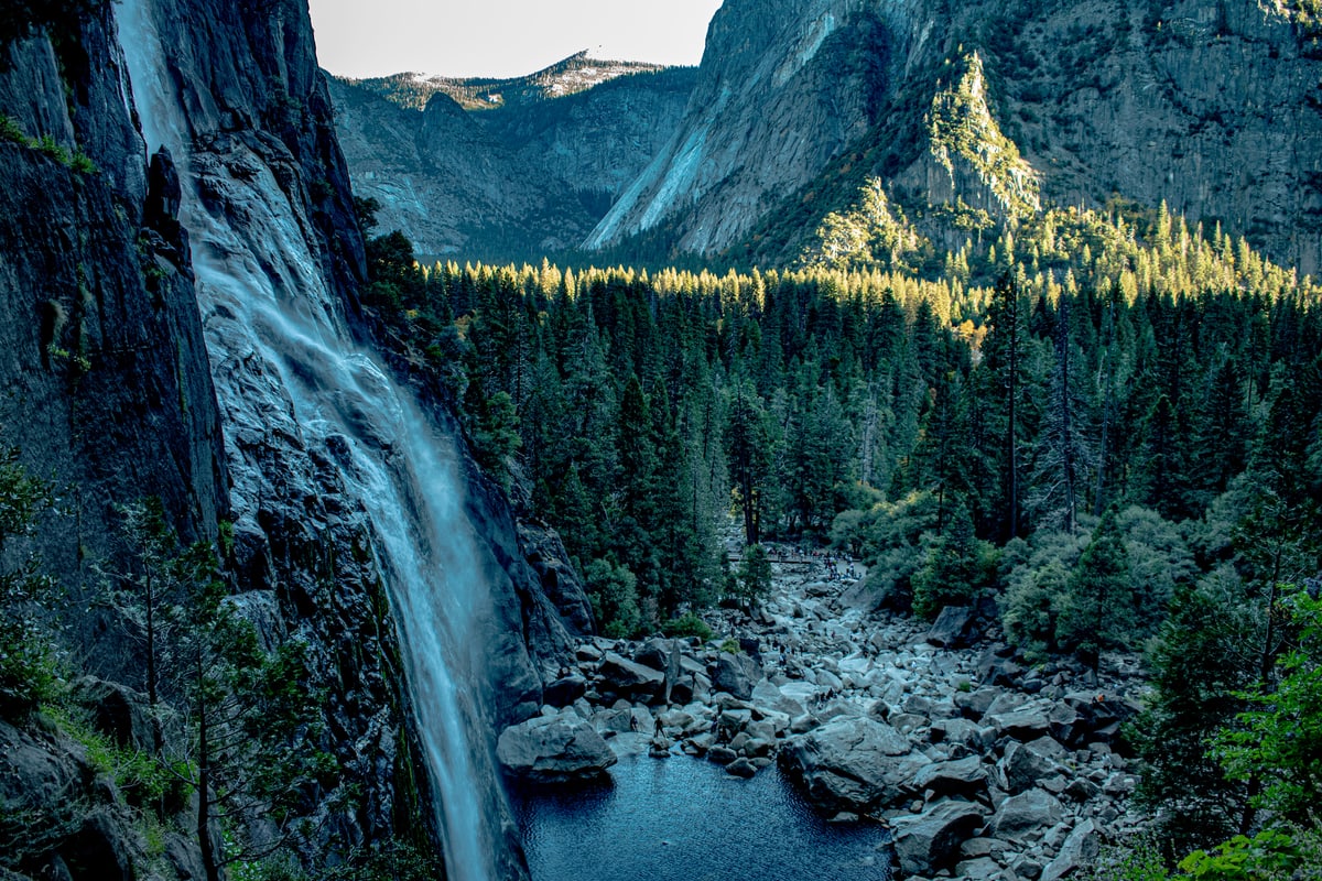 A waterfall pours down a granite cliff into a boulder-filled river in Yosemite.