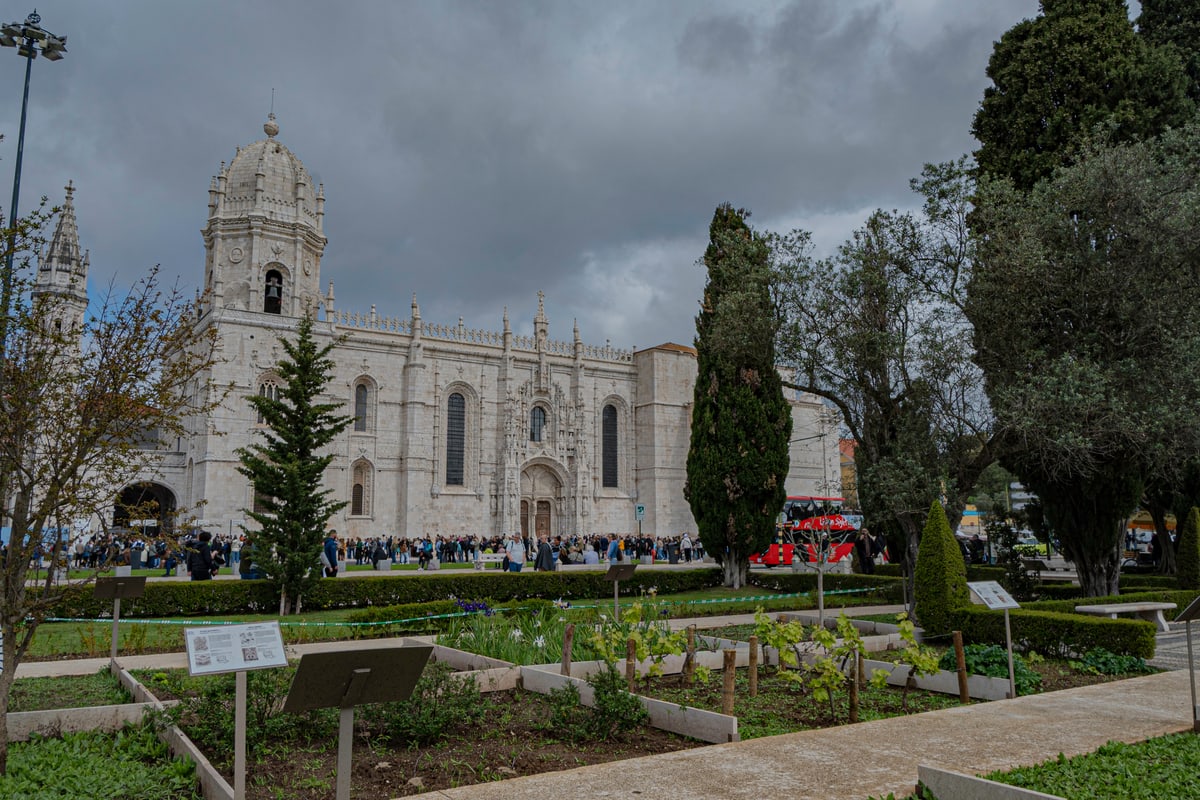 The ornate white facade of Jerónimos Monastery behind cypress trees.