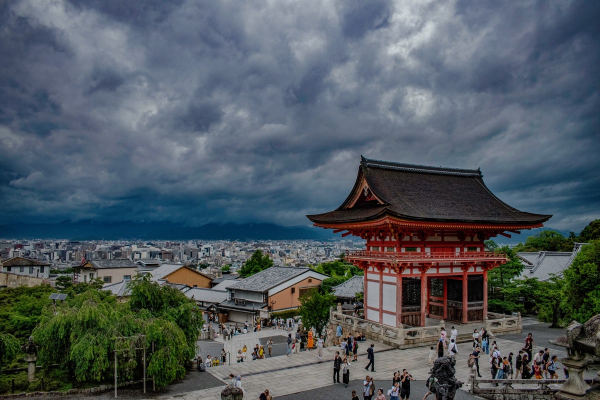 Kiyomizu-dera's vermilion gate under dark storm clouds above Kyoto.