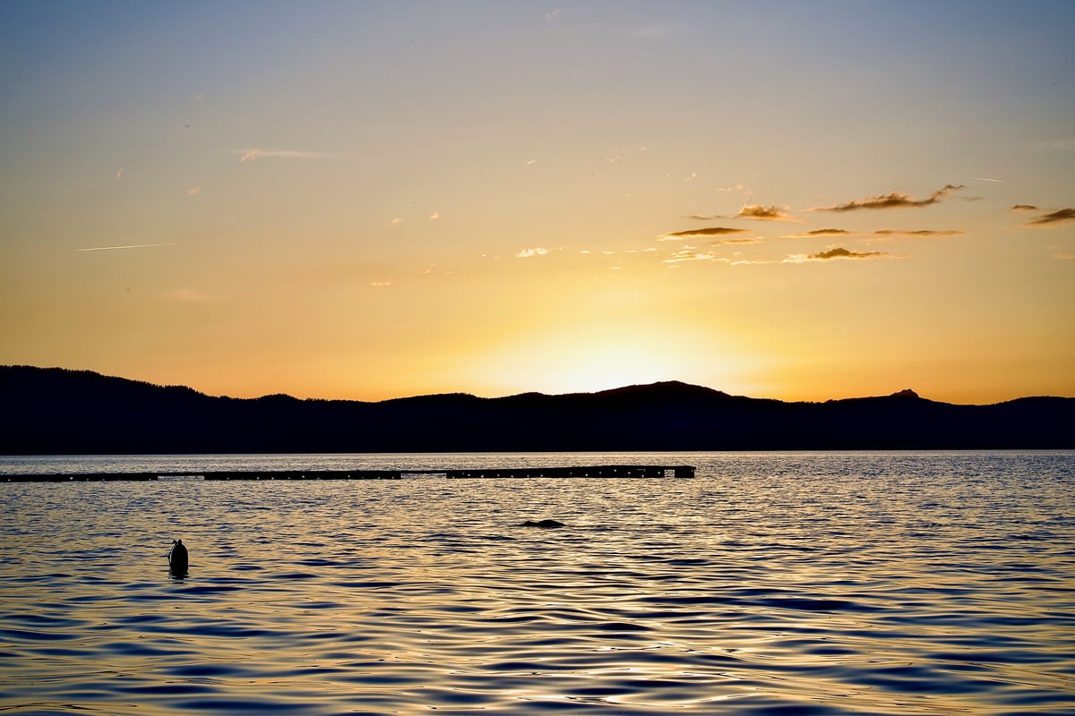 The sun sinks behind dark mountains over rippling lake water.