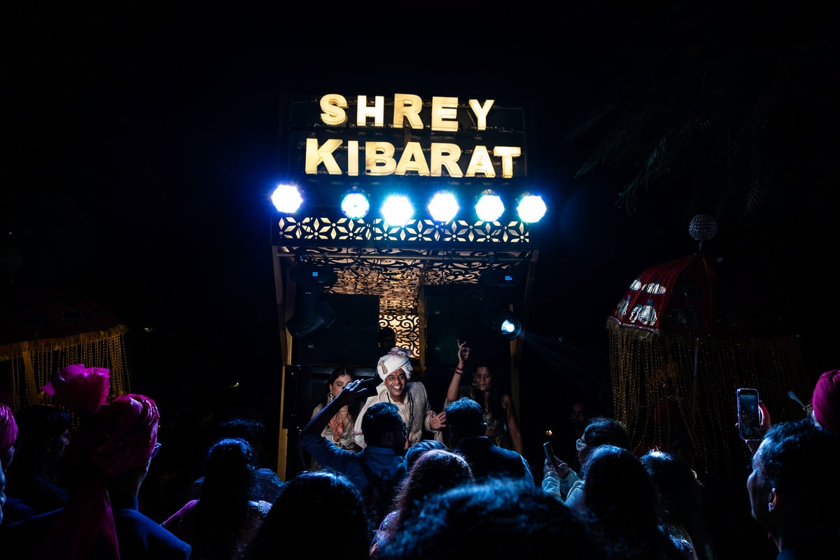 A crowd dances beneath a glowing sign during the baraat procession.