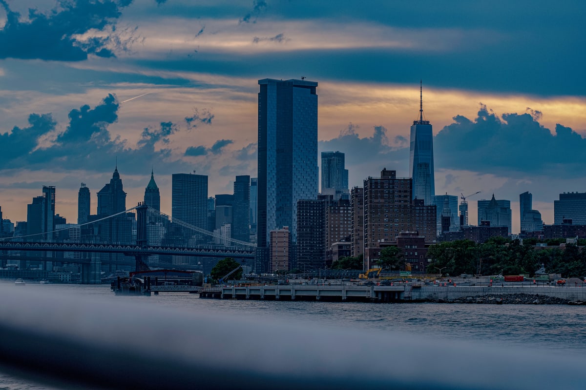 Lower Manhattan's skyline under moody clouds, seen across the water.