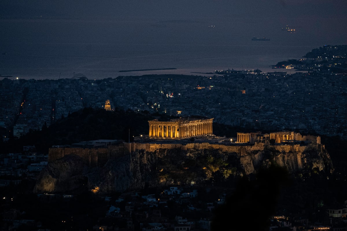 The Parthenon glows gold on the Acropolis above the dark city at night.