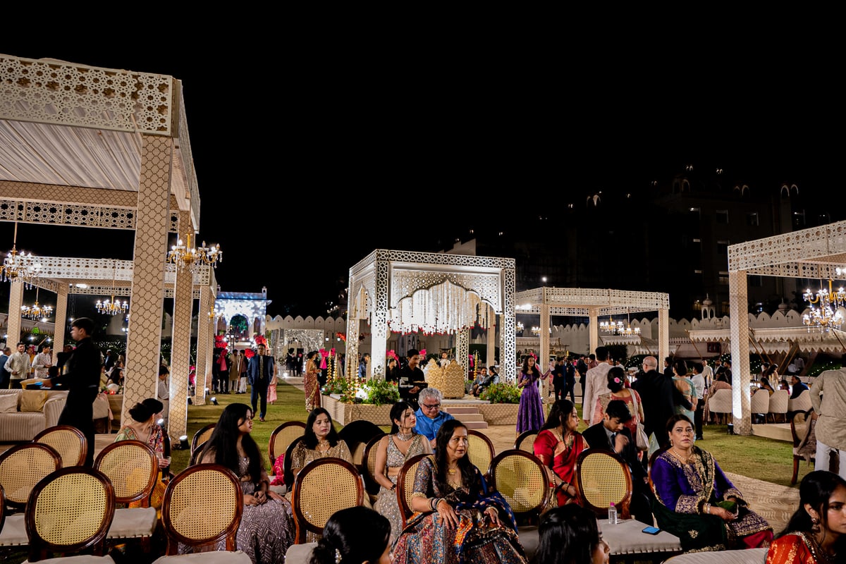 Guests seated among white carved pavilions in a palace courtyard at night.