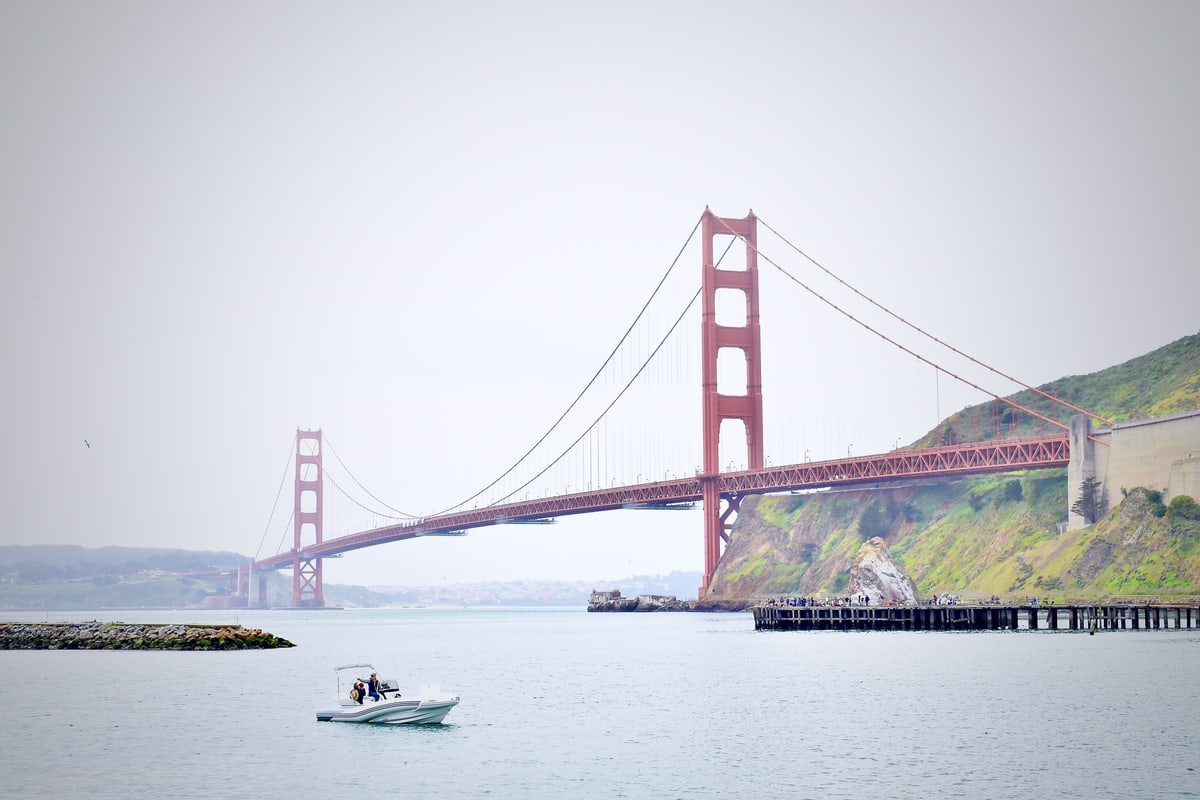 The Golden Gate Bridge stretches across the bay on a soft grey day as a small boat passes.