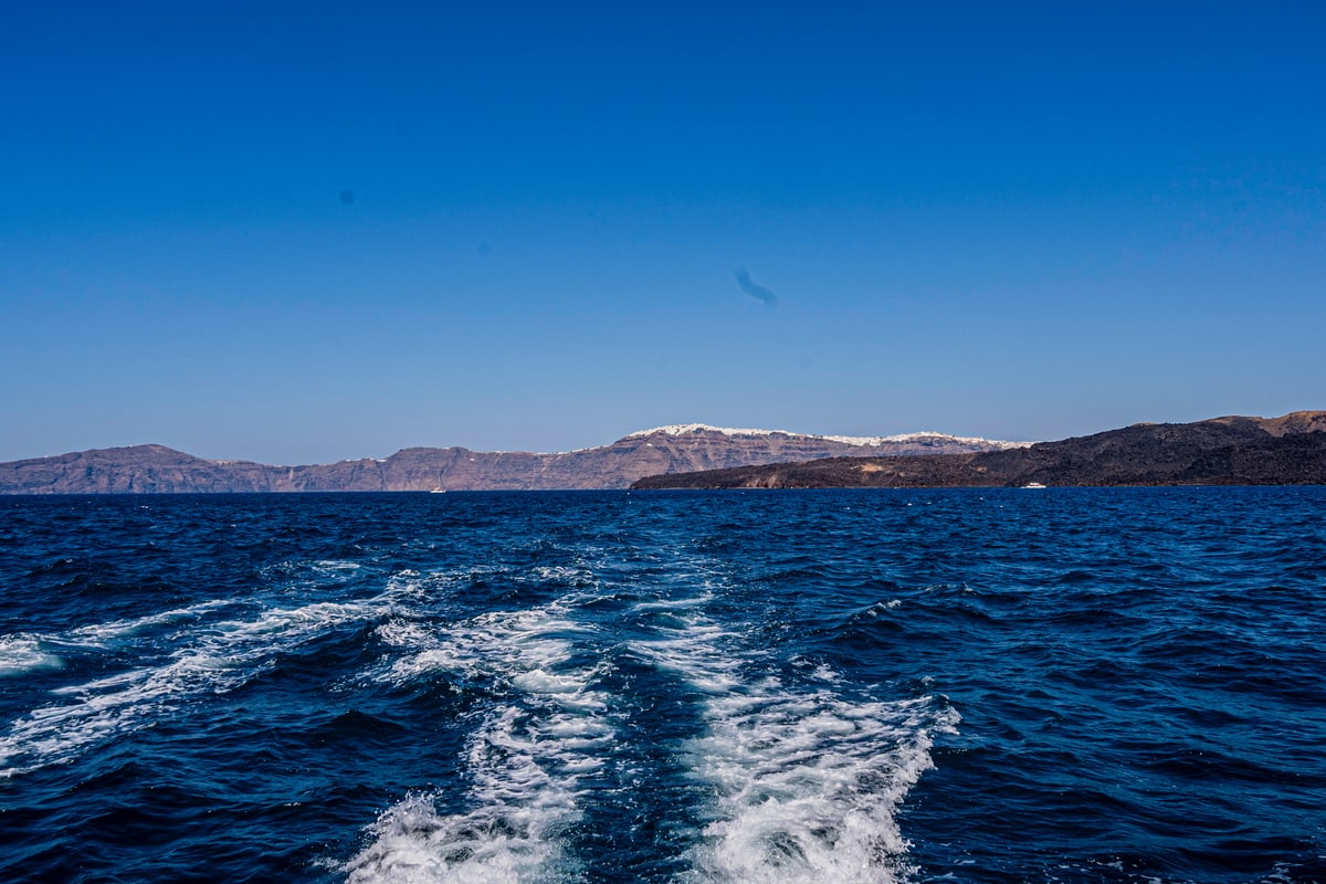 A boat's white wake trails across deep blue water toward distant islands.