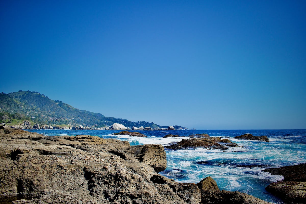 Waves crash against rocky outcrops along a rugged coastline.