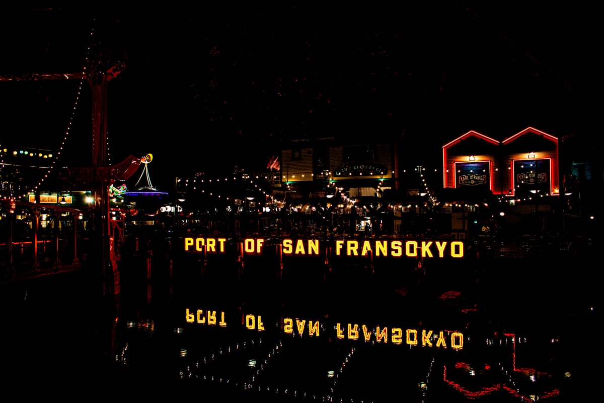 A lit San Fransokyo sign reflected in still black water.