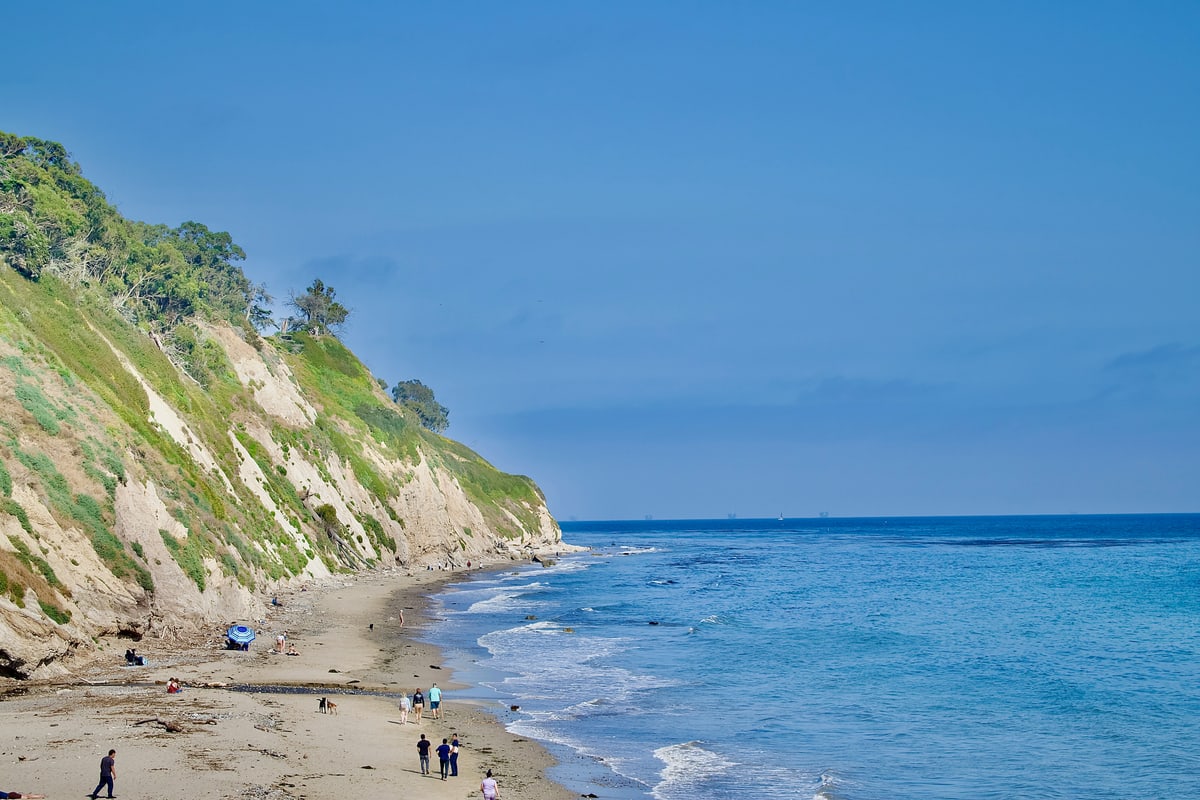 Green bluffs drop to a sandy beach and bright blue water.