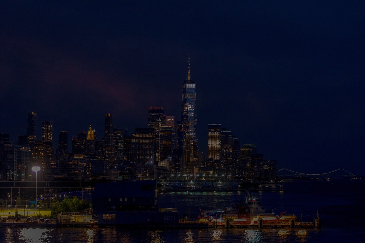 The Manhattan skyline at night reflected in dark water.