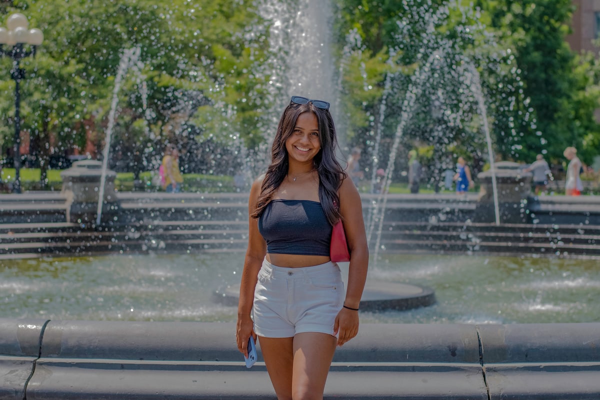 A woman walks toward the camera in front of the Washington Square Park fountain.