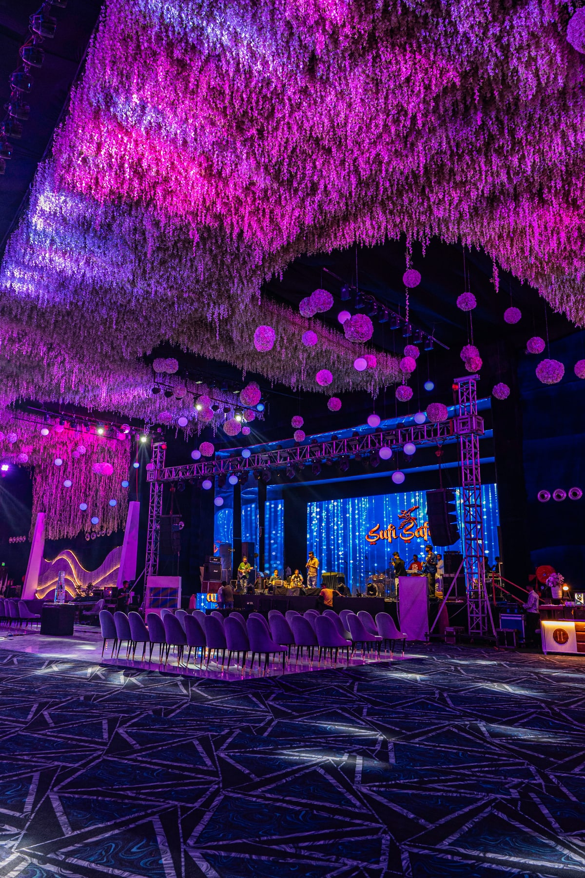 The reception stage lit in blue and pink beneath cascading floral decor.