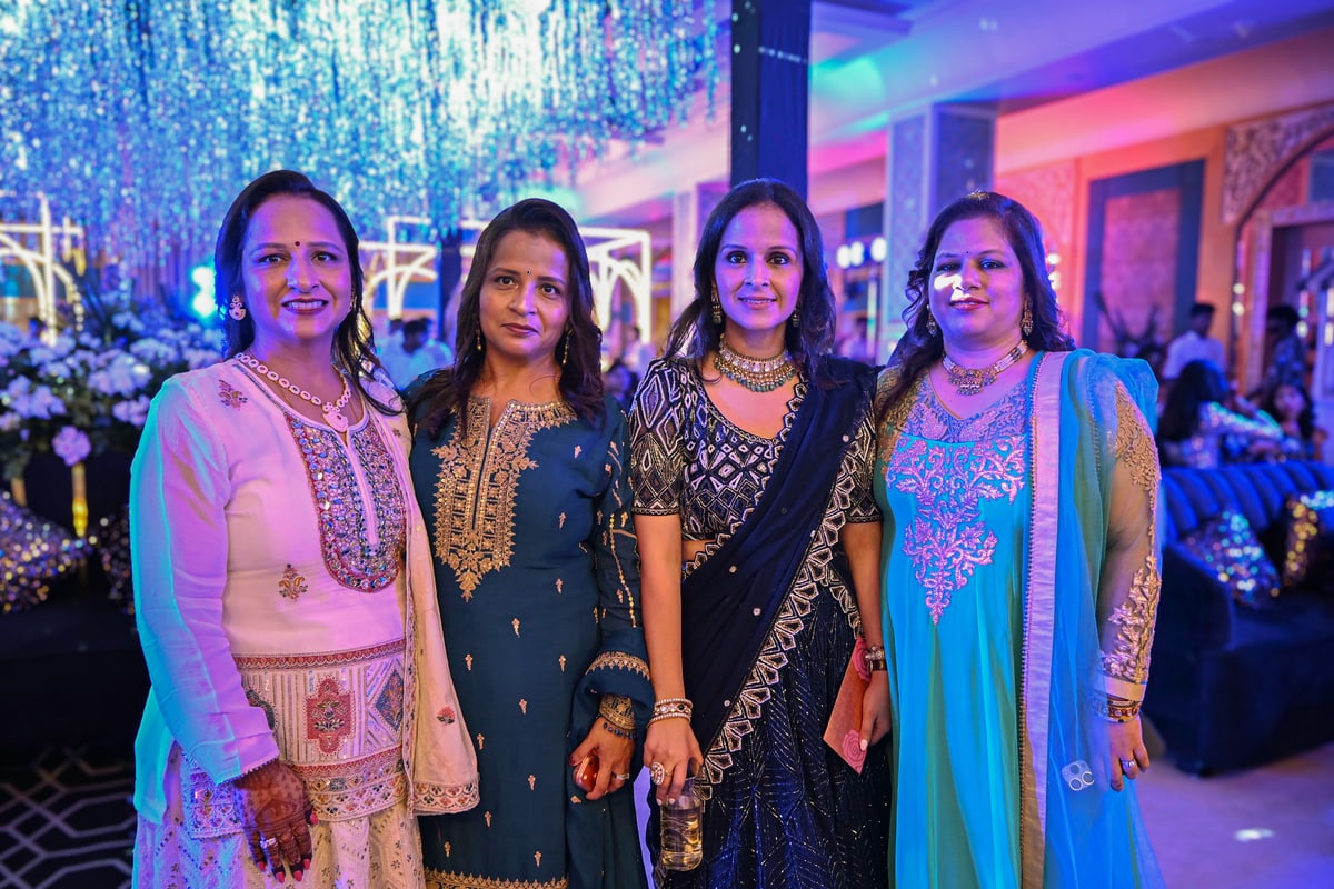 Four women in embroidered outfits smile together at the reception.