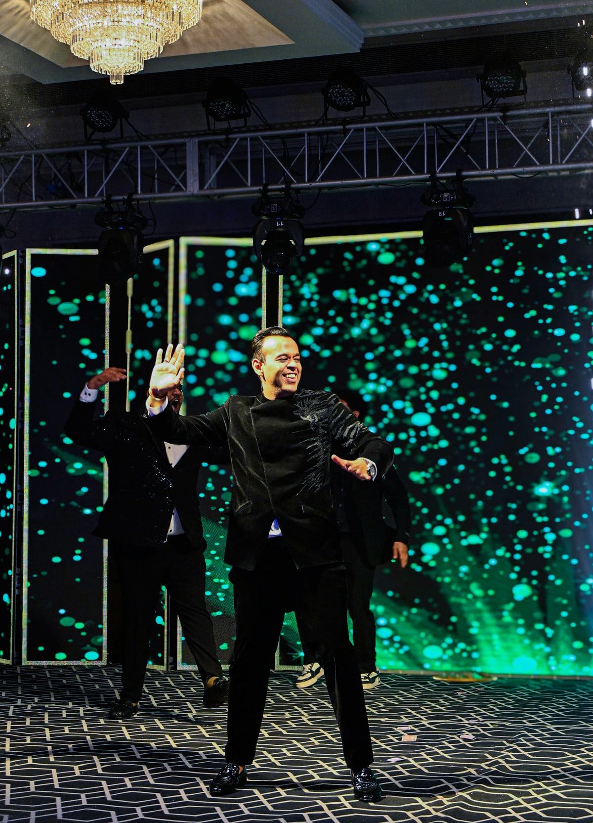A guest dances with his arms raised in front of a sparkling LED wall.