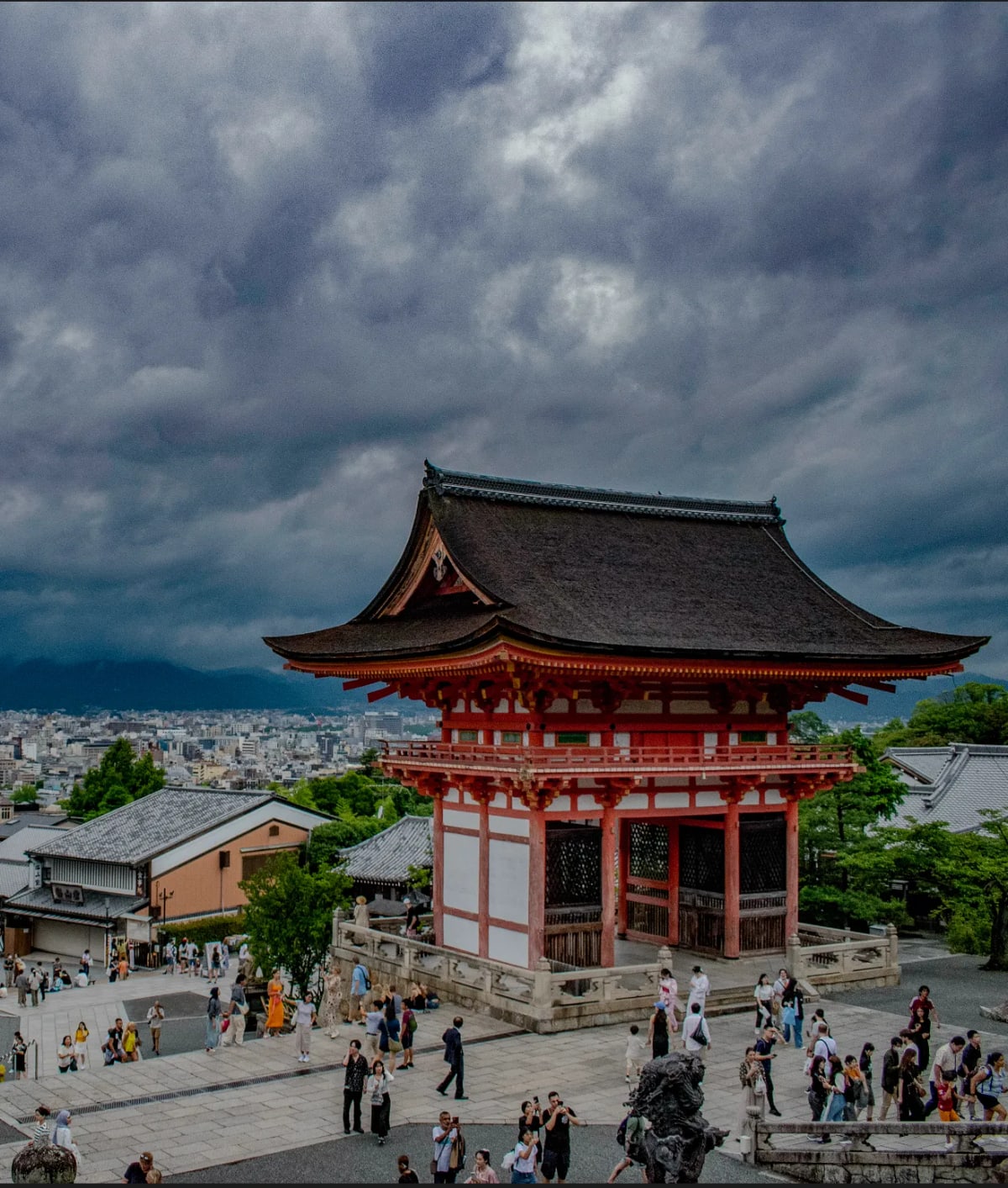 Kiyomizu-dera's vermilion gate under dark storm clouds above Kyoto.