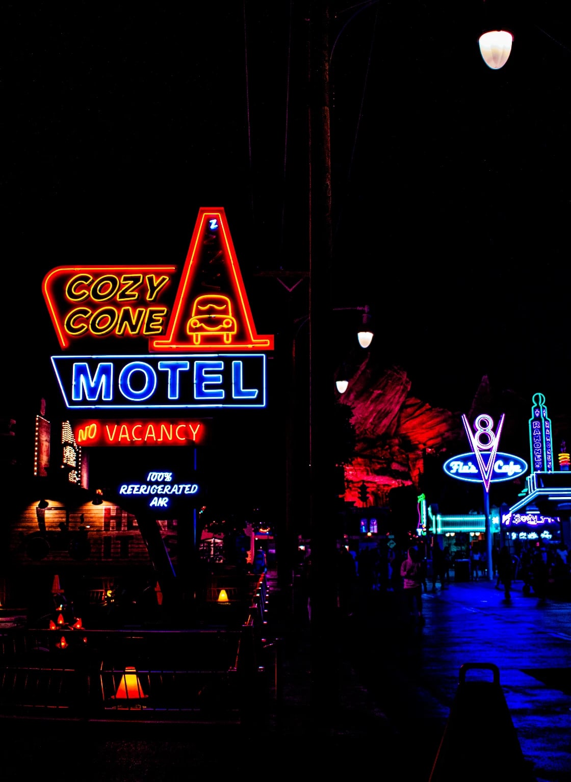 The Cozy Cone Motel and Flo's V8 Cafe neon signs glowing on a dark street at night.